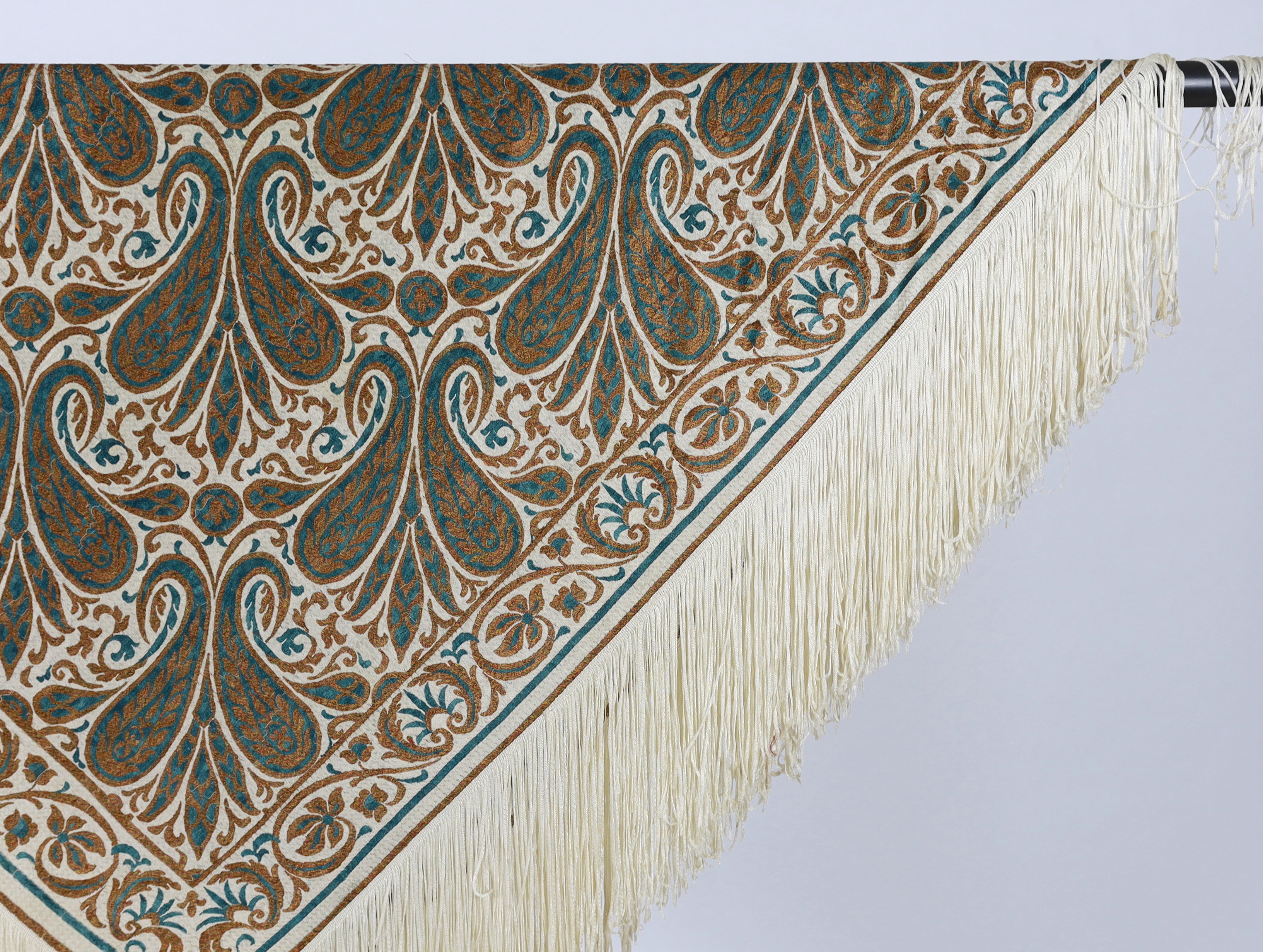 A 1920’s-1930’s cream silk woven shawl, woven with turquoise and bronze coloured silks in an all over tear drop paisley motif, edged with fine knitted cream fringing, approximately 109cm x 120cm